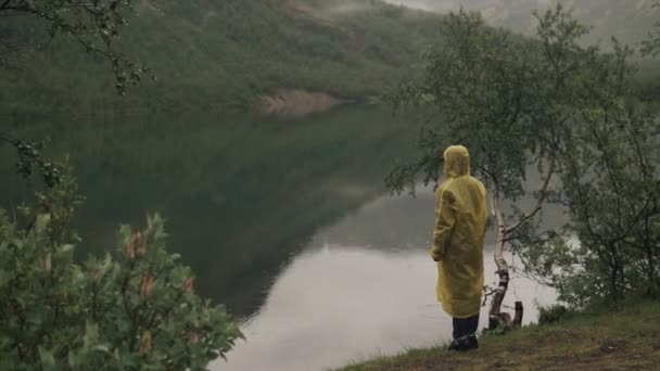 Una solitaria figura encapuchada estaba junto al lago con una capa amarilla. Solo. — Vídeos de Stock