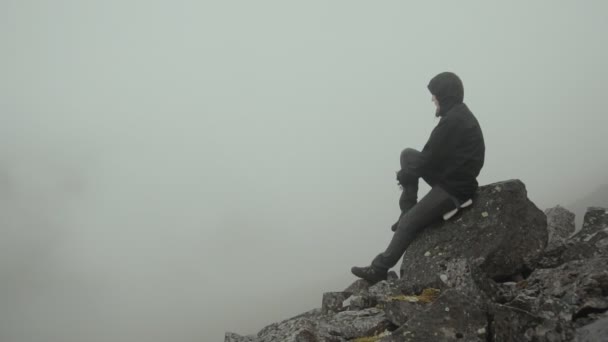 Одинокая фигура, сидящая на камне в пасмурный день — стоковое видео