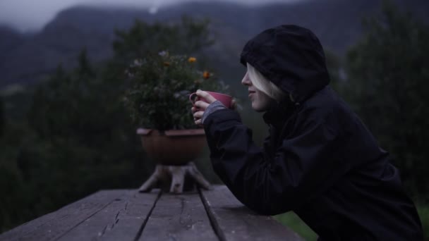 A kapucnis lány ül és teázik esténként a hegyekben. — Stock videók