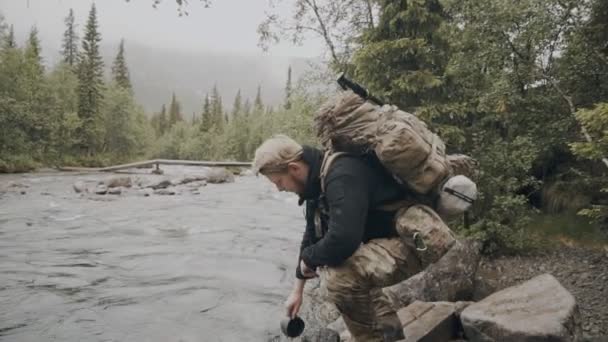 Turysta pije wodę ze strumienia górskiego. Podróżnik cieszy się czystą, nieskażoną wodą w górskiej rzece — Wideo stockowe