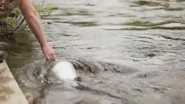 Un joven toma agua limpia de un arroyo de montaña en un cubo . — Vídeo de stock