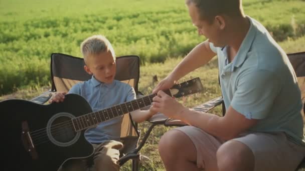 Ojciec uczy syna grać na gitarze na świeżym powietrzu. Zwolniony ruch — Wideo stockowe