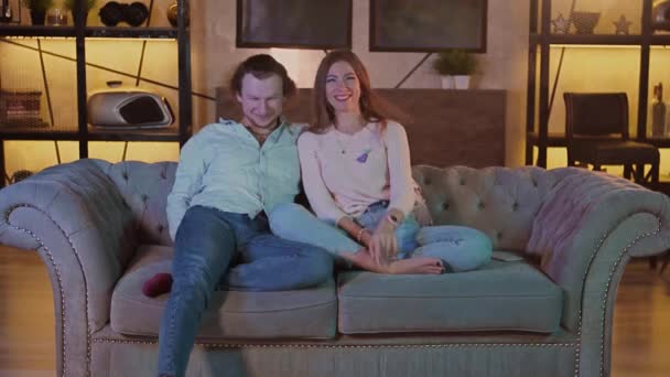 Młoda szczęśliwa atrakcyjna para zabawia się w domu oglądając telewizję razem w domu — Wideo stockowe
