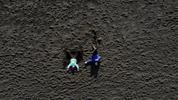 Deux personnes se trouvent sur le sable noir d'une plage. Océan Atlantique en Islande . — Video