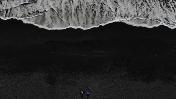 Vista aérea de duas pessoas sentadas na praia com areia preta . — Vídeo de Stock