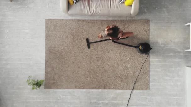 Ansicht von oben. Junge Frau staubt Teppich zu Hause ab — Stockvideo