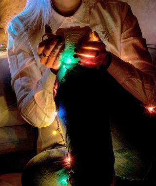 Bir fincan kahve, tutan eller çay. Noel ve yılbaşı ışıkları çelenk.