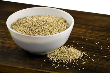 Bir ahşap tahta üzerinde beyaz bir kase içinde ham quinoa