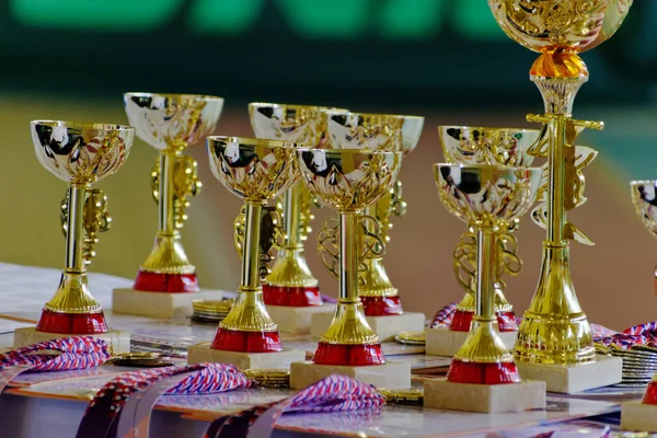 Altın şampiyon kupa ve madalya satırları dizilmiş. Bardak masanın üzerine altın spor.