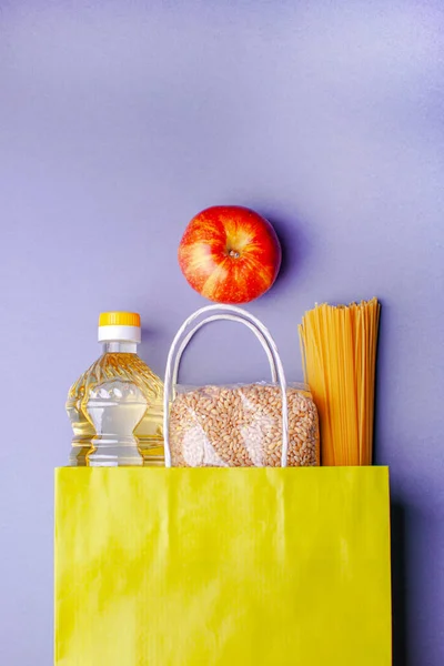 Food supplies for quarantine on lilac background. Pasta, fruits, sunflower oil, cereals. Food box. Food delivery, donation.