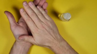 Sarı arka planda dezenfektanla el temizleyen kişinin kısmi üst görünümü