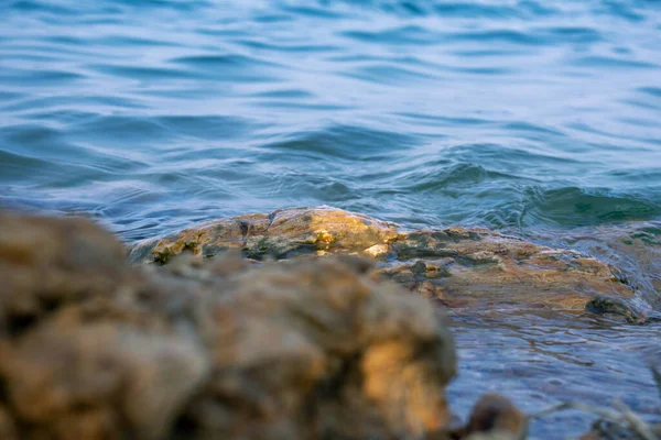 stock image small waves cutting the rocks in the shore of a blue lake