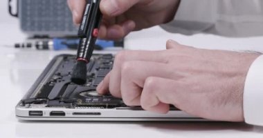 4K 'da beyaz duvarlı laboratuvarda fırçayla toz dizüstü bilgisayarın ana kart devre soğutucusunu tamir eden servis çalışanı.