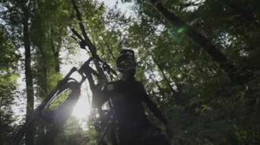 Dağ bisikletçisi bisikletini ormanda ağır çekimde taşıyor.