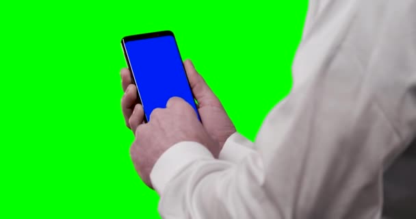身穿白衬衫 手持智能手机 背景为蓝色调和绿色屏幕的男子 使用社交媒体刷卡并双击 — 图库视频影像