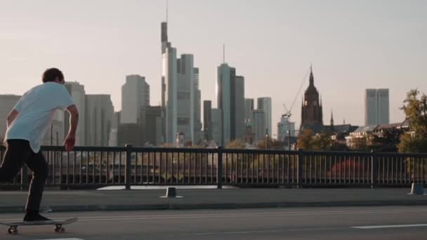 フランクフルトの高層ビル群の前で超スローモーションで橋を渡るスケートボーダー — ストック動画