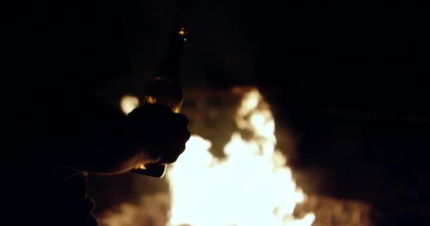 燃えるキャンプファイヤーの前でビールを保持男スローモーション4K — ストック動画