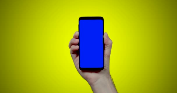 Mann Hält Smartphone Mit Blauem Chroma Schlüssel Auf Gelbem Hintergrund — Stockvideo