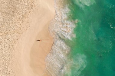 Bir kız okyanus kıyısında uzanır dron yeşili okyanustan Nusa Penida Bali Kelingking plajından 