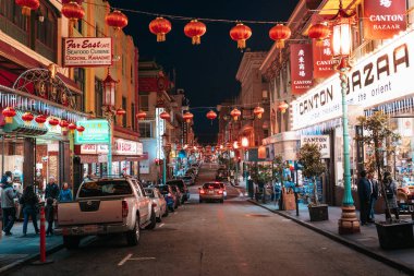 San Francisco 'daki Çin Mahallesi' nin bir caddesinde. Çin gece lambaları caddeyi aydınlatıyor, cadde boyunca dükkanların ve restoranların işaretleri var.