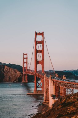 Gün batımında San Francisco 'da muhteşem bir milli anıtın ve tarihi Golden Gate Köprüsü' nün fotoğrafı. Dünyanın en ünlü köprüsünün altında küçük tekneler yelken açıyor.
