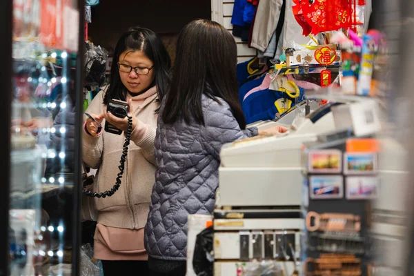 两名亚洲妇女在礼品店工作 一个女人手里拿着一个终端用信用卡付款 — 图库照片