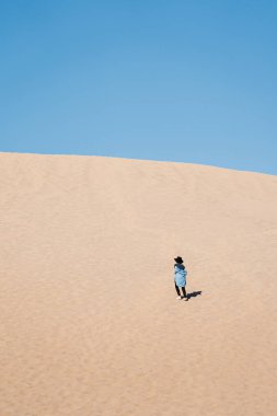 Seyahat eden bir kız kumulun tepesinde kameraya doğru koşuyor. Ölüm Vadisi Milli Parkı 'nda siyah şapkalı ve mavi etekli bir gezgin.
