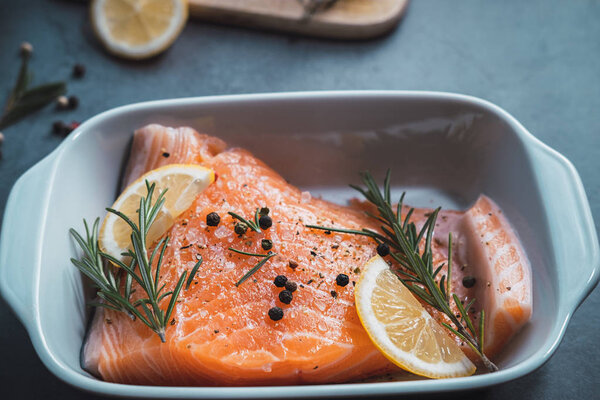 Fresh raw salmon ready for the oven with rosemary, lemon, pepper and salt.
