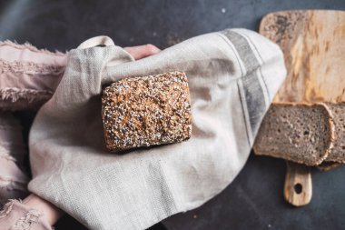 Eller çok çekirdekli ekmek ve arka planda dilimler tutuyor.. 