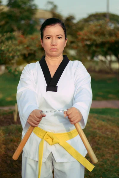 Kolumbianische, lateinamerikanische Frau praktiziert Taekwondo mit Nunchakus in Startposition — Stockfoto