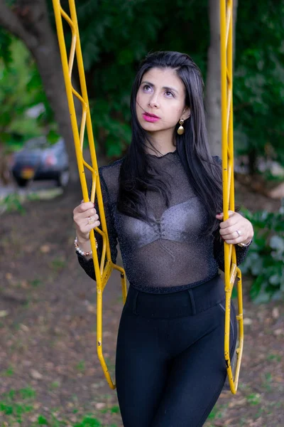 Mujer colombiana disfrutando de una tarde soleada en el parque de la ciudad jugando en el columpio —  Fotos de Stock