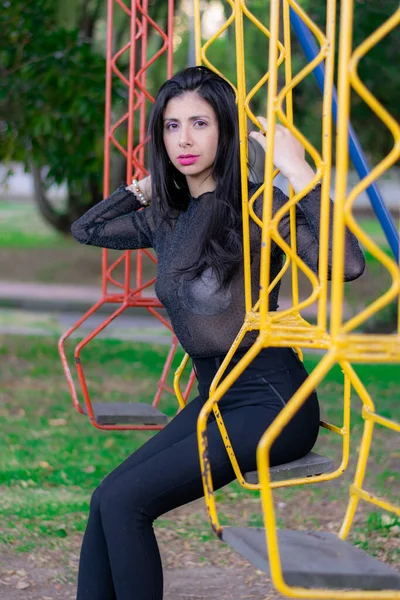 Mujer colombiana disfrutando de una tarde soleada en el parque de la ciudad jugando en el columpio —  Fotos de Stock