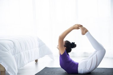 Zayıf, genç bir kadın yoga odasındaki Asana 'da sakince ve rahat bir şekilde oturuyor. Pencerenin arkasındaki ışık sabahları hafif ve rahattır. Sağlık hizmeti kavramı