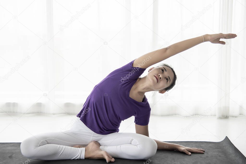 woman slim, young teen  sits on the asana in the yoga room calmly and relaxed. The light behind the window is light and comfortable in the morning. Concept of health care