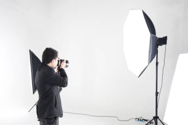 Asyalı profesyonel fotoğrafçı şirketin stüdyosunda beyaz arka planda ışıklandırma ekipmanıyla fotoğraf çekmeye hazırlanıyor. İmaj satışı konsepti günümüzde popüler..