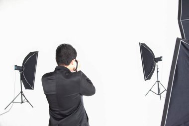 Asyalı profesyonel fotoğrafçı şirketin stüdyosunda beyaz arka planda ışıklandırma ekipmanıyla fotoğraf çekmeye hazırlanıyor. İmaj satışı konsepti günümüzde popüler..