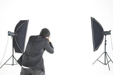 Asyalı profesyonel fotoğrafçı şirketin stüdyosunda beyaz arka planda ışıklandırma ekipmanıyla fotoğraf çekmeye hazırlanıyor. İmaj satışı konsepti günümüzde popüler..