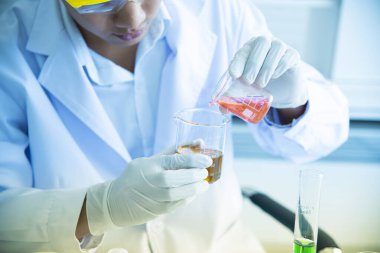 Asyalı genç bilim adamı, kimyasalların üretiminde kullanılmasını araştırıyor ve test ediyor. Bilim laboratuvarlarında test tüpleri, icatlar ve araştırma kavramları.