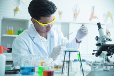 Asyalı genç bilim adamı, kimyasalların üretiminde kullanılmasını araştırıyor ve test ediyor. Bilim laboratuvarlarında test tüpleri, icatlar ve araştırma kavramları.