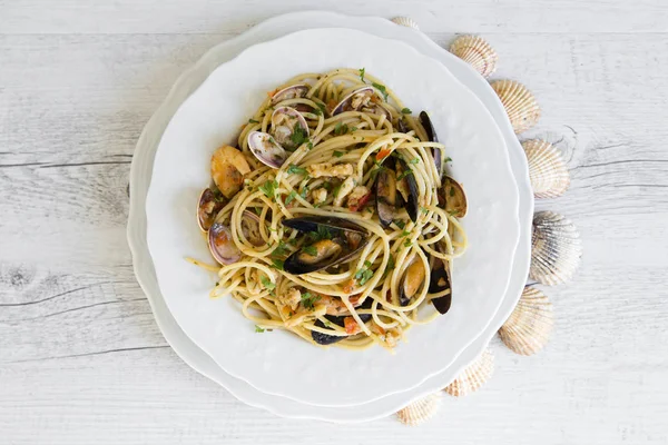 Espaguetis con mariscos en placa de cerámica blanca sobre fondo de madera — Foto de Stock