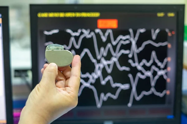 Doctor Hand hold Pacemaker device with screen of EKG monitoring background