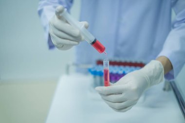 Biyolog tüpün içine sıvı kan bırakıyor, laboratuvarda çalışıyor. Tıbbi teknisyen laboratuarda test için tüplerde kan örneği tutuyor..