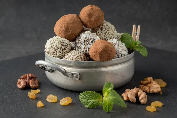 Energy bites with cocoa powder, sesame seeds and coconut flakes in small saucepan on grey table