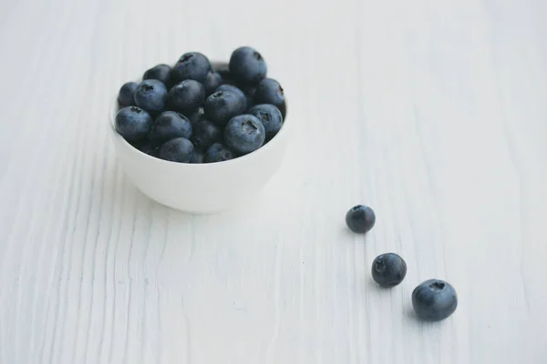 Blaubeeren in einer weißen Schüssel auf einem hölzernen Hintergrund — Stockfoto