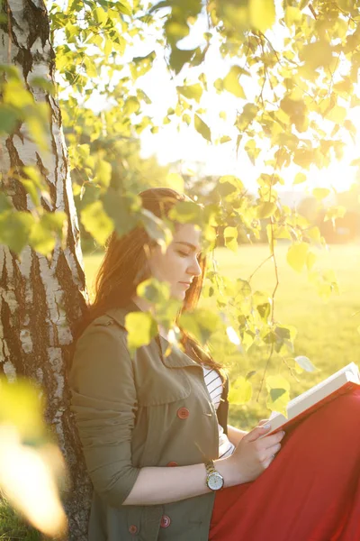 Jonge vrouw zit met een boek onder een boom op een zonnige dag — Stockfoto