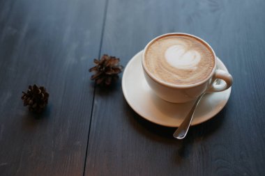 Sıcak kapuçino, koyu ahşap arka planda kurutulmuş koniler.