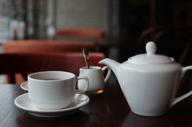 Koyu ahşap zemin üzerinde bir fincan siyah çay ile beyaz çaydanlık.