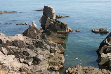 sunny lonely beach with deep blooming water and boulders and rocks 