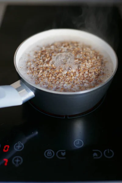 boiling buckwheat in saucepan on electric black stove with glossy surface