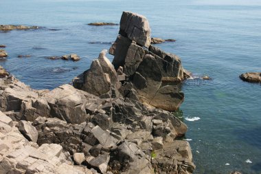 sunny lonely beach with deep blooming water and boulders and rocks 